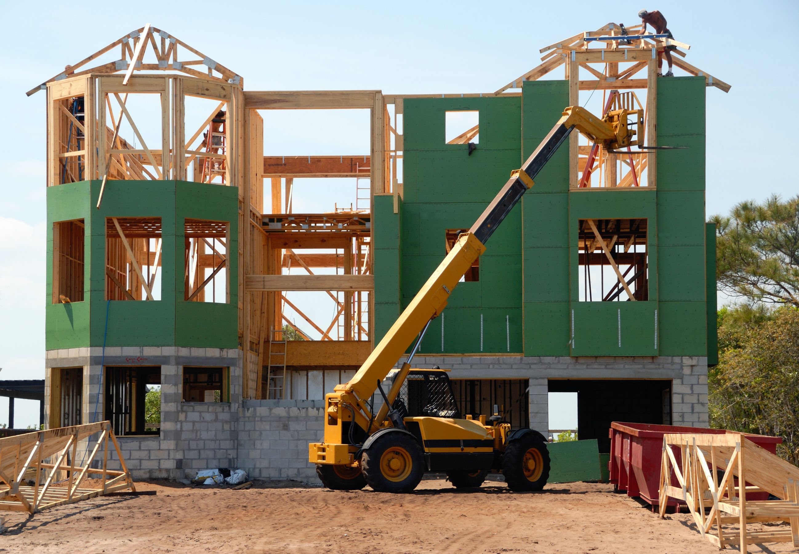 A three-story house being framed, with a telehandler on site